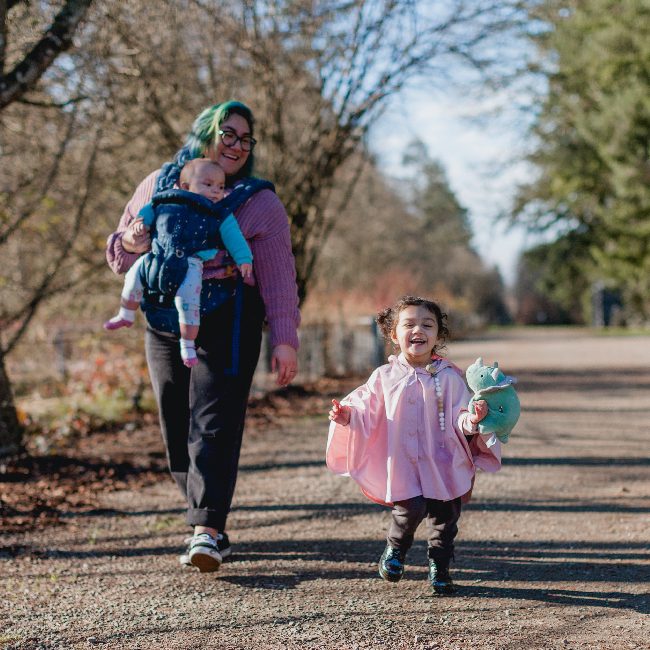 A mother on a walk with her child and a baby in a baby shoulder sling.