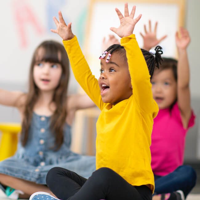 A group of children smiling and raising their hands in the air