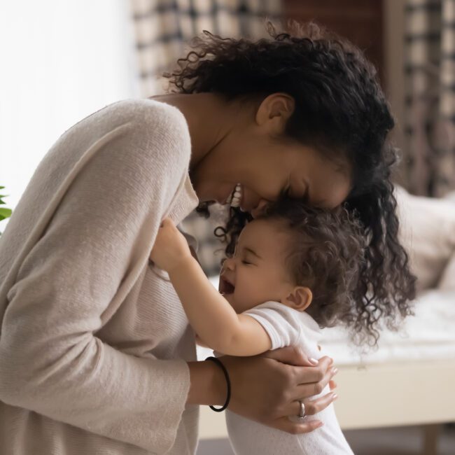 Happy loving young Black mother embraces infant at home