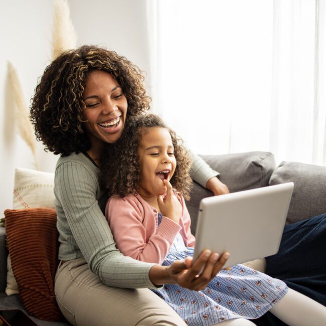 Mother and daughter sitting on the sofa and using digital tablet for video call with grandparents