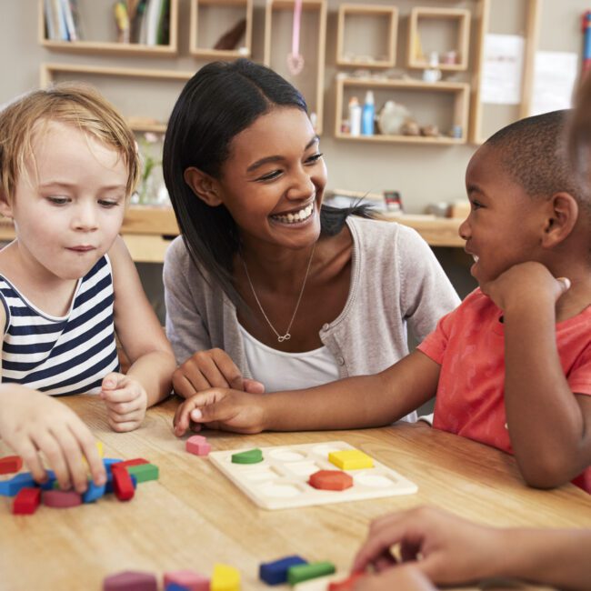 Teacher And Pupils Using Wooden Shapes In Montessori School