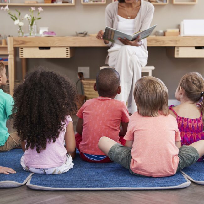 Teacher At Montessori School Reading To Children At Story Time