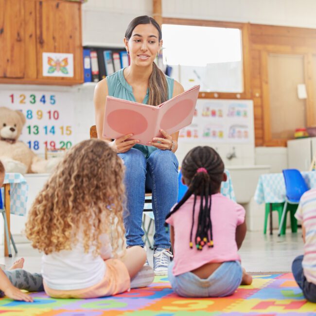 Shot of a young woman reading to her preschool students